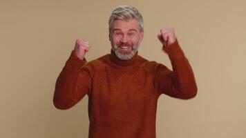Middle-aged mature old man shouting, raising fists in gesture I did it, celebrating success, winning video