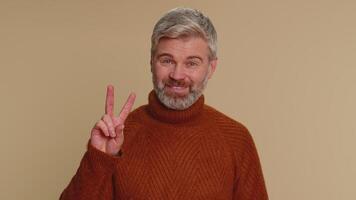 Middle-aged optimistic old man showing victory sign, hoping for success and win, doing peace gesture video