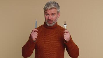 Hungry middle-aged man with fork, knife waiting for serving dinner dishes with cutlery, meal lunch video