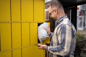Man retrieving package from bright yellow locker in urban setting photo