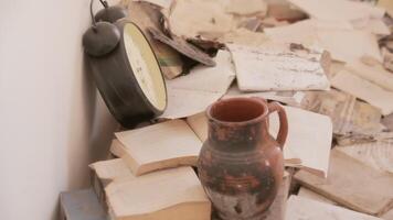 Piles of old books and a broken alarm clock inside a room, into an abandoned house. The hand of a man browsing the pages. video