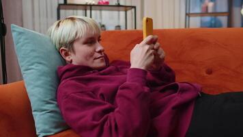 Portrait of young woman lying on sofa, using smartphone share messages on social media application video
