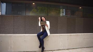 A chic and stylish modern woman is casually using her laptop outdoors in a lively urban setting video