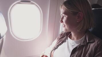 Passenger woman is flying in plane. Girl sitting in airplane looking out window going on trip vacation travel. Traveling female inside plane enjoying flight. Traveling girl video