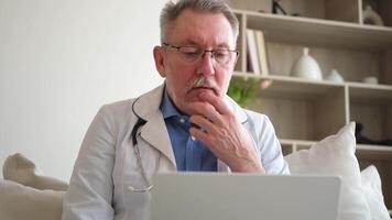 Senior man doctor working with laptop computer. Professional senior mature healthcare expert searching information or have online consultation in hospital room. Medicine healthcare medical checkup video