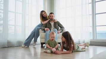 Happy family at home. Mother father two children daughters relaxing indoor. Mom dad parents baby girls kids relax playing having fun together. Family smiling laughing enjoying tender love moment video