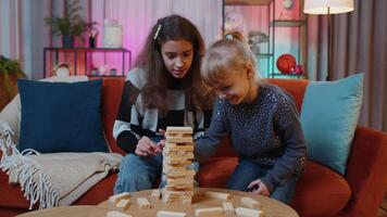 Siblings children girls playing with blocks, board game, build tower from wooden bricks at home video
