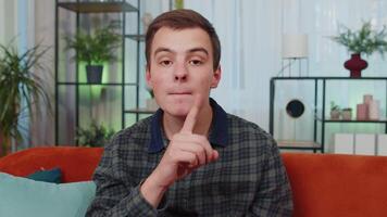 Young man presses finger to lips makes silence hush sign do not tells gossip secret, quiet at home video