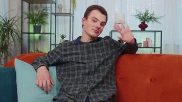 Teenager man smiling friendly at camera, waving hands gesturing hello, hi, greeting at home on couch video