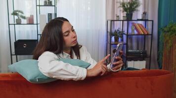 Portrait of adult girl sitting on sofa, using smartphone share messages on social media application video