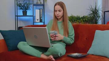 Smiling happy girl counting money cash and use laptop pc calculate domestic income earnings at home video
