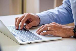 Businessman hand work on capable laptop computer at office table close up shot and selective focus at middle section of laptop computer keyboard while typing and working photo