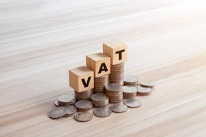 VAT word in wooden blocks with coins stacked in increasing stacks. Vat increasing concept. Copy space photo