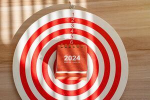 close up 2024 small calendar on dartboard, red dart arrow hitting photo