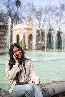 vertical Latin girl talking on the cell phone and having a coffee photo