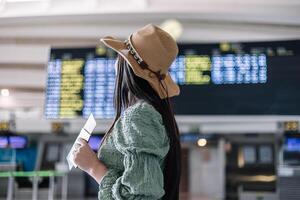 closeup from behind latin girl with passport in hand looking at information board in terminal photo