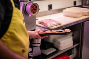 Closeup of Butcher's Hands Carrying Tray of Freshly Prepared Chicken Nuggets, with Detailed View of Meat Grinding Machine in Background photo