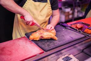 Closeup of Butcher's Hands in Yellow Apron Cutting Chicken for Customer at Butcher Shop Counter photo