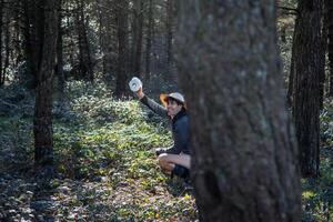 Young camper defecating behind tree trunk in forest while holding toilet paper roll photo