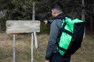 Hiker Points Towards Informative Sign Amidst Forest Exploration photo