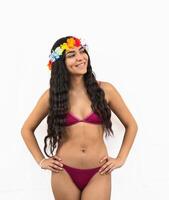 Smiling Latin woman posing in bikini with hands on hips and flower crown, enjoying summer on white background photo