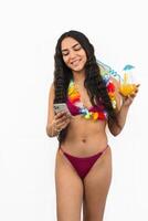 vertical portrait Latin girl texting on smartphone in bikini and flower necklace on white background photo