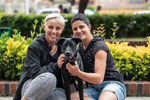 Lesbian couple and their dog posing for a photo in the garden, looking at the camera