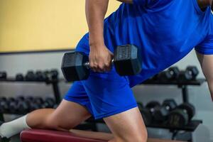 close-up of anonymous person doing triceps exercise with dumbbell on gym bench photo