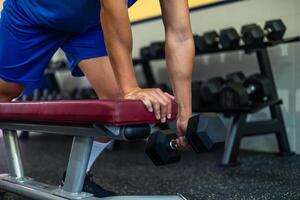 close-up of anonymous athlete holding weight dumbbell while exercising on gym bench photo