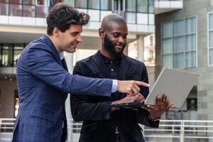 African businessman holds laptop while Hispanic colleague points at screen to emphasize data photo