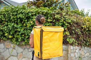 Hispanic food delivery girl with backpack, seen from behind, walking to complete her delivery job photo