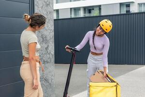 Latin courier with yellow helmet and electric scooter taking package from backpack for customer photo
