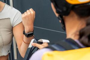 unrecognized courier with yellow helmet holding payment terminal while client pays with smartwatch photo