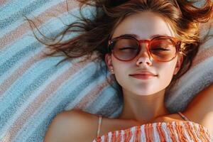 Young woman relaxing on a beach towel under the sun with sunglasses on a warm summer day photo