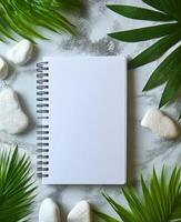 Blank notebook surrounded by greenery and stones on a marble surface for creative inspiration photo