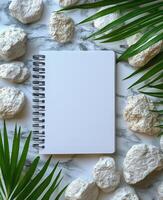 Blank notebook surrounded by greenery and stones on a marble surface for creative inspiration photo