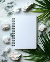 Blank notebook surrounded by greenery and stones on a marble surface for creative inspiration photo