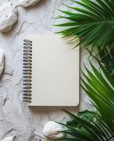 Blank notebook surrounded by greenery and stones on a marble surface for creative inspiration photo