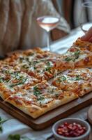 Deliciously cheesy pizza on a wooden board with fresh herbs and ros wine nearby photo