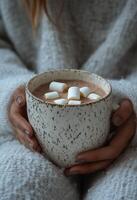Warm cozy drink with marshmallows held by a person in soft textured sweater indoors during winter photo