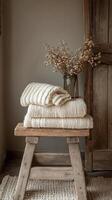 Cozy knitted blankets and dried flowers arranged at a rustic wooden stool in a warm setting photo