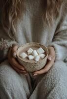 Warm cozy drink with marshmallows held by a person in soft textured sweater indoors during winter photo