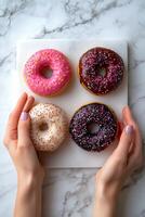 Hands holding three colorful donuts with sprinkles on a marble background photo