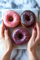 Hands holding three colorful donuts with sprinkles on a marble background photo