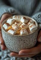Warm cozy drink with marshmallows held by a person in soft textured sweater indoors during winter photo