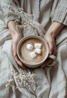 Warm cozy drink with marshmallows held by a person in soft textured sweater indoors during winter photo