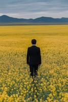 Man walking through vibrant yellow field towards distant hills during sunset photo