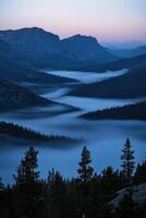 Misty valley landscape at twilight with mountains in the background and dense forest photo
