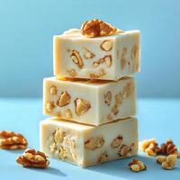 Creamy walnut confection stacked on a blue surface with additional nuts scattered around photo