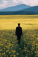 Man walking through vibrant yellow field towards distant hills during sunset photo